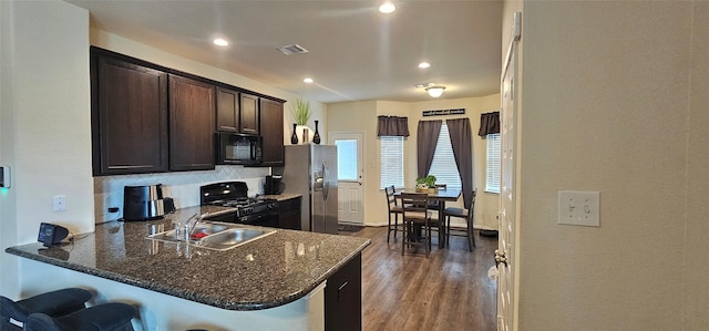 kitchen featuring a breakfast bar area, visible vents, a sink, black appliances, and dark brown cabinetry