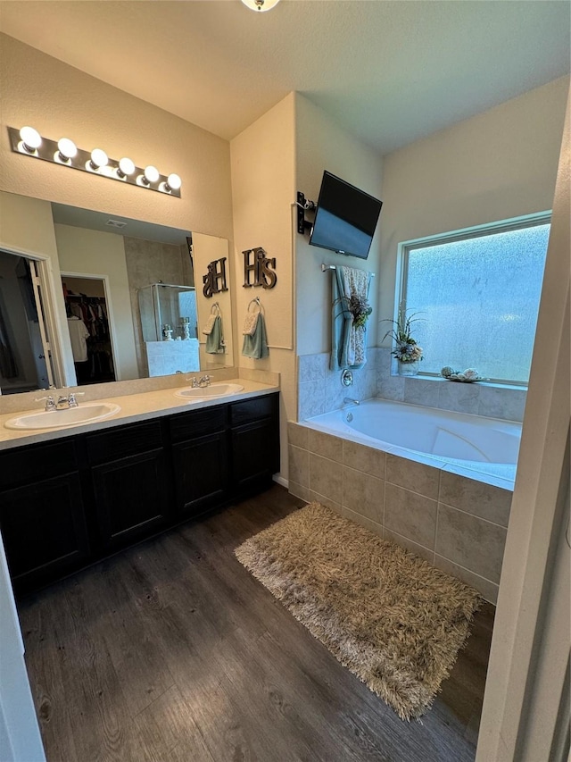 full bath featuring a shower stall, a walk in closet, a garden tub, wood finished floors, and a sink