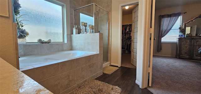 full bath featuring a spacious closet, a shower stall, baseboards, a garden tub, and wood finished floors