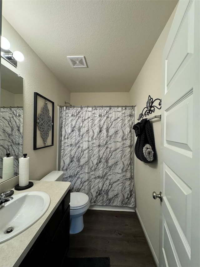 bathroom with visible vents, toilet, a textured ceiling, wood finished floors, and vanity