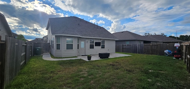 back of house with a yard, roof with shingles, a fenced backyard, and a patio area