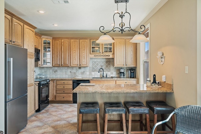 kitchen featuring light stone countertops, a kitchen bar, a peninsula, black appliances, and a sink