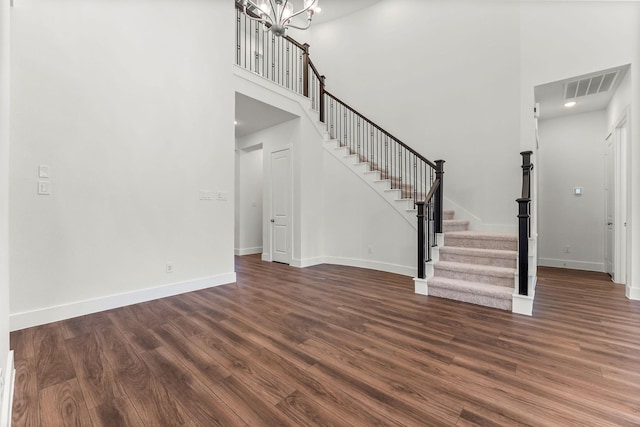 unfurnished living room with visible vents, baseboards, stairway, a towering ceiling, and dark wood-style floors