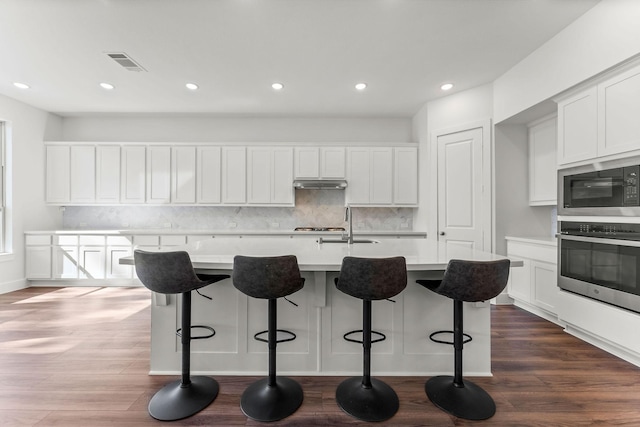 kitchen with oven, visible vents, dark wood-type flooring, and built in microwave