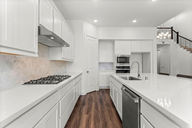 kitchen with under cabinet range hood, a sink, an inviting chandelier, appliances with stainless steel finishes, and dark wood-style flooring