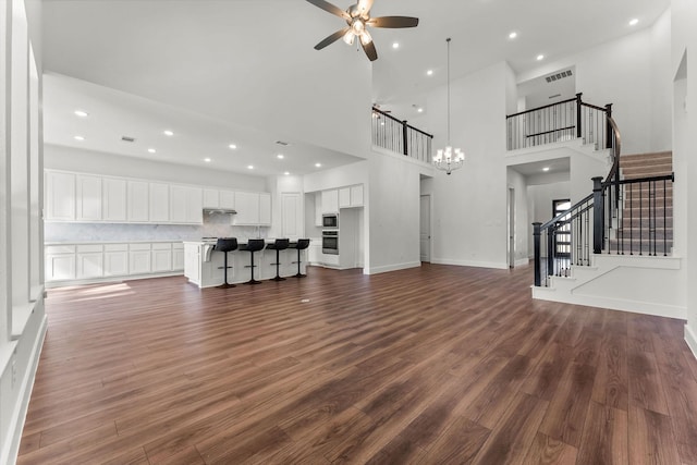 unfurnished living room featuring visible vents, dark wood-type flooring, ceiling fan with notable chandelier, stairway, and baseboards