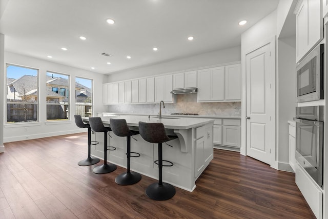 kitchen featuring oven, visible vents, under cabinet range hood, a sink, and built in microwave