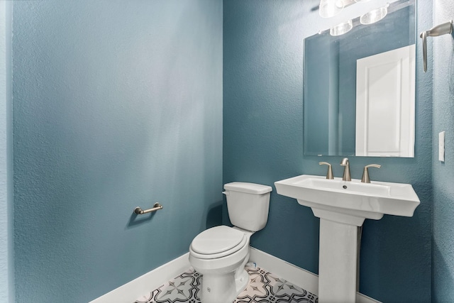 bathroom featuring baseboards, a sink, tile patterned flooring, toilet, and a textured wall