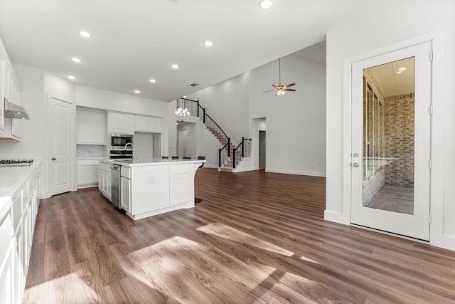 kitchen with a kitchen island with sink, stainless steel appliances, dark wood-type flooring, wall chimney exhaust hood, and open floor plan