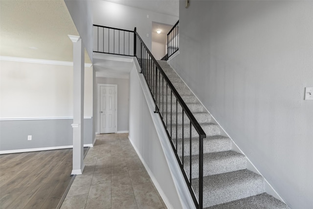 stairs with wood finished floors, baseboards, a towering ceiling, and ornamental molding