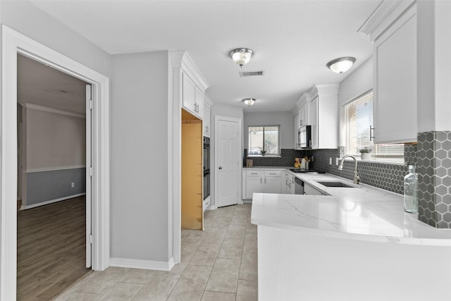 kitchen featuring visible vents, a sink, light stone counters, tasteful backsplash, and stainless steel appliances