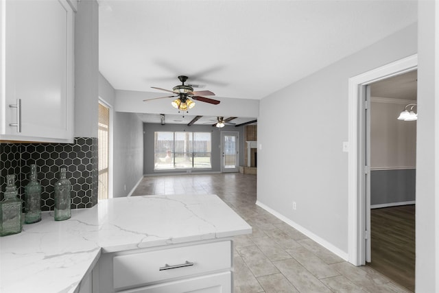 kitchen featuring light stone counters, a brick fireplace, a peninsula, and white cabinetry