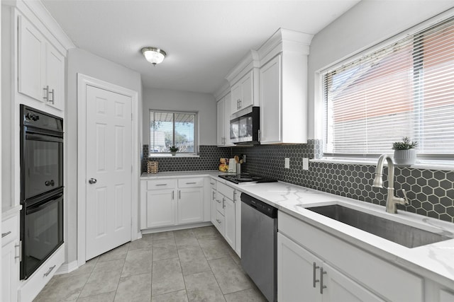 kitchen featuring light stone counters, a sink, black appliances, white cabinets, and backsplash