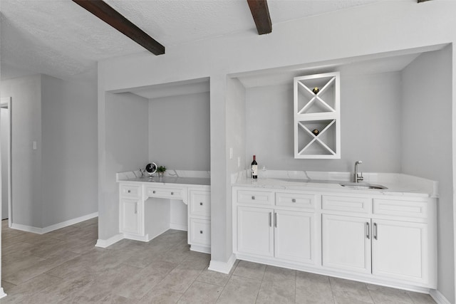 bar featuring wet bar, a sink, built in desk, a textured ceiling, and beamed ceiling