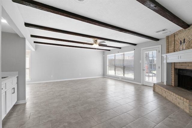 unfurnished living room with beamed ceiling, a textured ceiling, baseboards, a brick fireplace, and ceiling fan