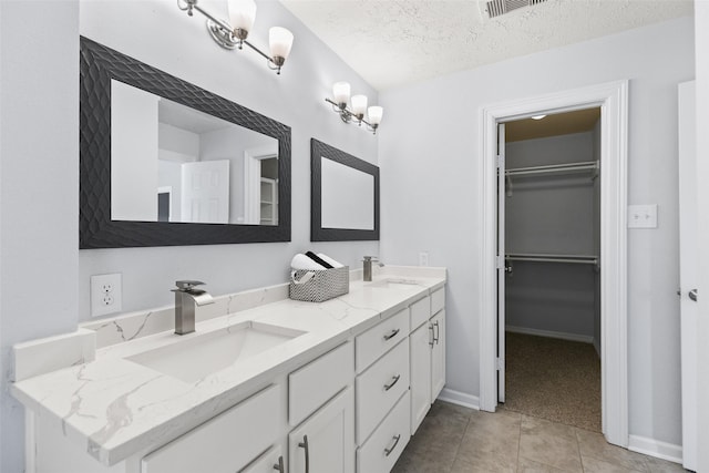 bathroom with a textured ceiling, double vanity, a spacious closet, and a sink