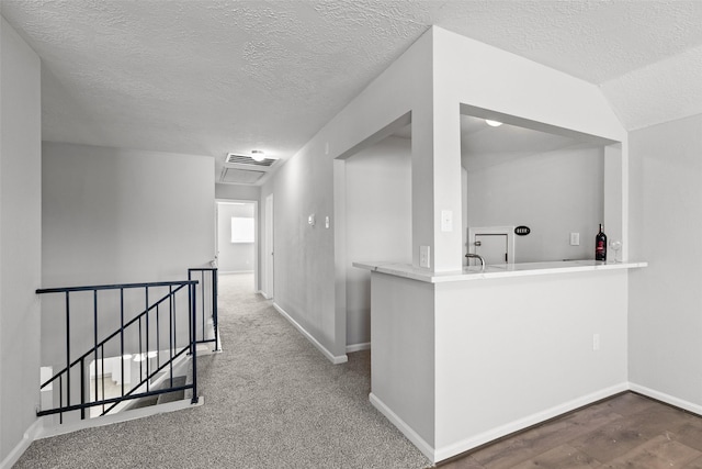 corridor with an upstairs landing, a textured ceiling, baseboards, and wood finished floors