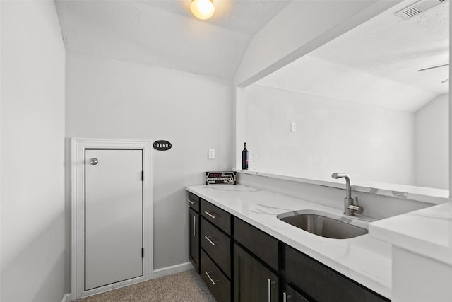 kitchen featuring dark cabinetry, light stone countertops, visible vents, a sink, and vaulted ceiling