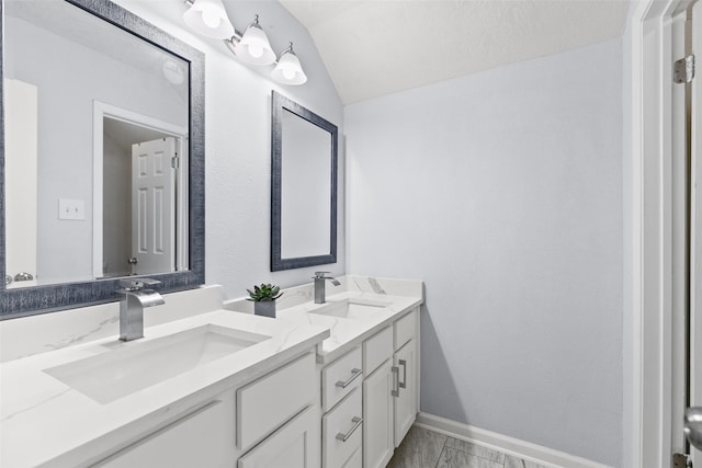 bathroom with a sink, baseboards, lofted ceiling, and double vanity