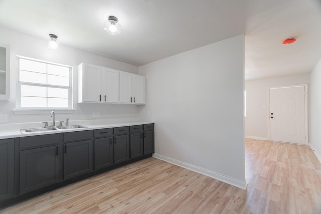 kitchen with a sink, baseboards, light wood-style flooring, and light countertops