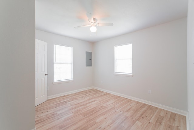 unfurnished room featuring electric panel, baseboards, light wood-style floors, and a healthy amount of sunlight