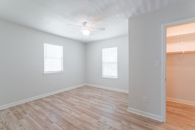 unfurnished bedroom with a walk in closet, multiple windows, and light wood finished floors