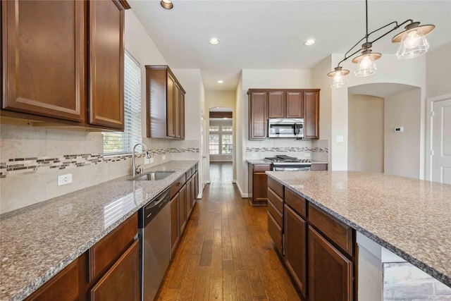 kitchen with light stone countertops, dark wood-style floors, appliances with stainless steel finishes, arched walkways, and a sink