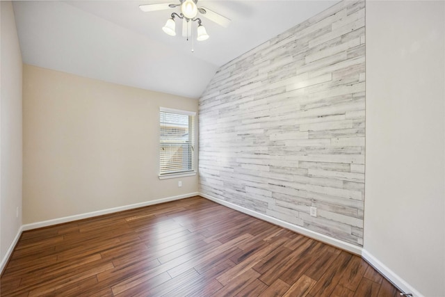 unfurnished room with wooden walls, wood finished floors, baseboards, ceiling fan, and vaulted ceiling