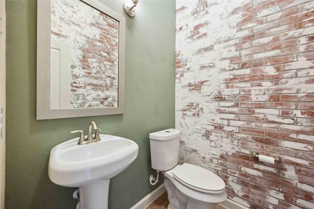 bathroom with a sink, baseboards, toilet, and brick wall