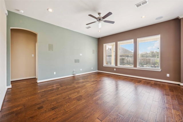 empty room featuring arched walkways, visible vents, a ceiling fan, and dark wood-style flooring