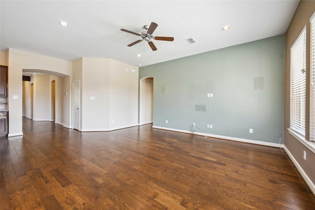 spare room featuring a wealth of natural light, baseboards, arched walkways, and dark wood-style flooring