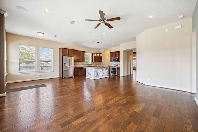 unfurnished living room featuring arched walkways, visible vents, a ceiling fan, and dark wood-style flooring