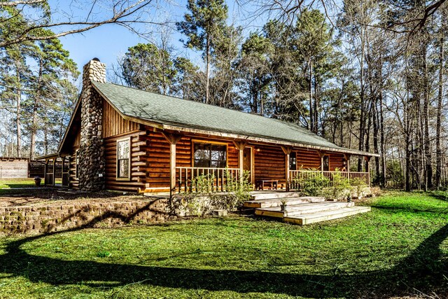 exterior space with a porch, a yard, a shingled roof, a chimney, and log exterior