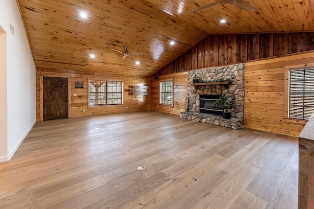 unfurnished living room with wood walls, a stone fireplace, wooden ceiling, wood finished floors, and a ceiling fan