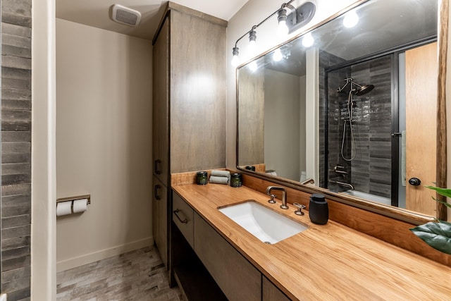 full bath featuring visible vents, baseboards, a tile shower, wood finished floors, and vanity