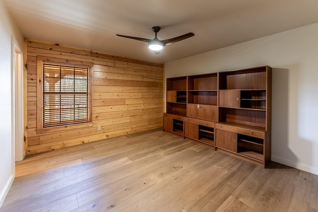 unfurnished living room with baseboards, light wood-style flooring, a ceiling fan, and wood walls