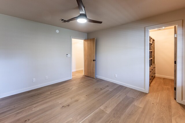 unfurnished bedroom with a spacious closet, ceiling fan, light wood-type flooring, and baseboards