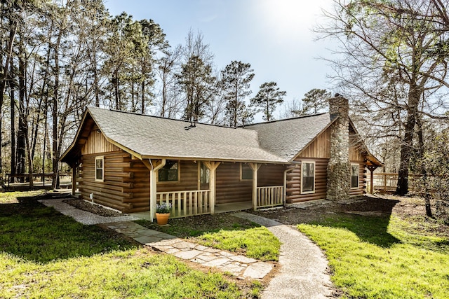 view of front facade with a front lawn, a porch, log exterior, roof with shingles, and a chimney