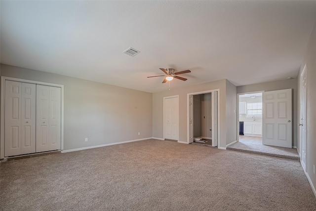 unfurnished bedroom featuring visible vents, multiple closets, baseboards, and carpet flooring