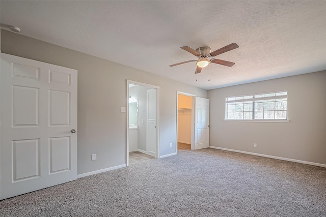 unfurnished bedroom with a walk in closet, baseboards, carpet floors, and a textured ceiling