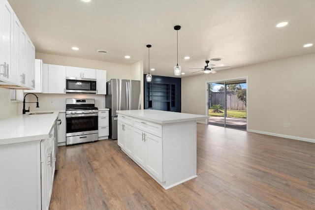 kitchen with a sink, wood finished floors, appliances with stainless steel finishes, white cabinets, and ceiling fan