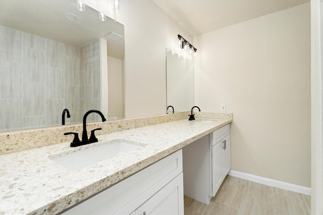 bathroom featuring double vanity, a tile shower, baseboards, and a sink