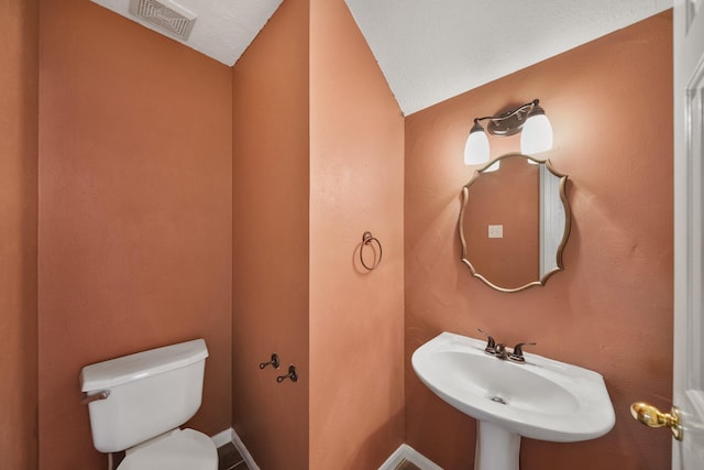 half bathroom with a sink, visible vents, baseboards, and toilet