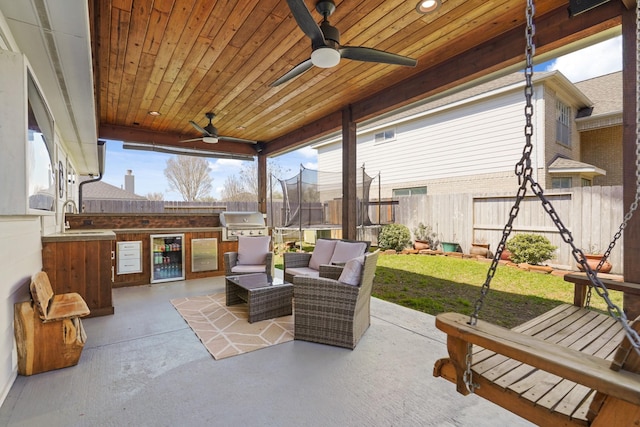 view of patio / terrace featuring area for grilling, a fenced backyard, ceiling fan, wine cooler, and a trampoline