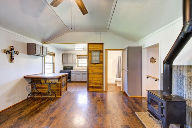 kitchen with electric range, a wood stove, ceiling fan, dark wood-type flooring, and vaulted ceiling