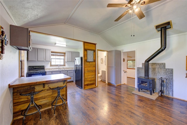 kitchen with lofted ceiling, a wood stove, gray cabinets, freestanding refrigerator, and range with electric stovetop