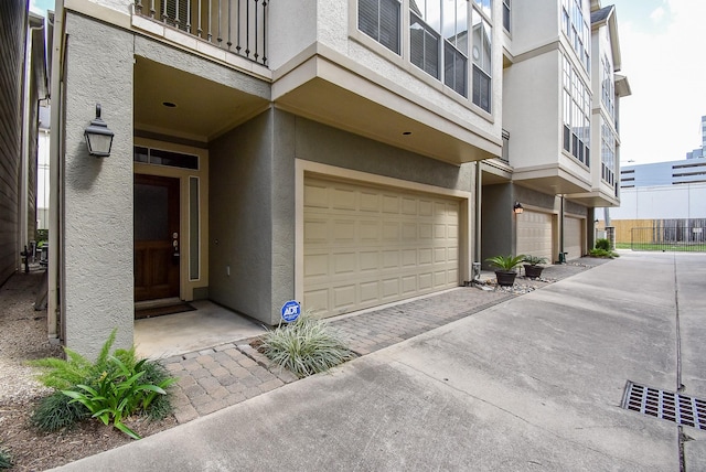 view of exterior entry featuring stucco siding, an attached garage, driveway, and a balcony