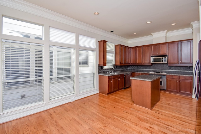 kitchen with a sink, a center island, stainless steel appliances, light wood finished floors, and decorative backsplash