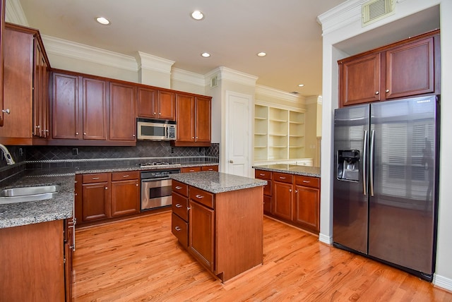 kitchen with light wood-type flooring, a sink, a kitchen island, dark stone counters, and appliances with stainless steel finishes