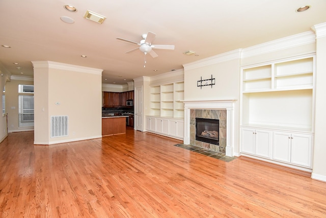 unfurnished living room featuring a tiled fireplace, visible vents, light wood-style flooring, and crown molding